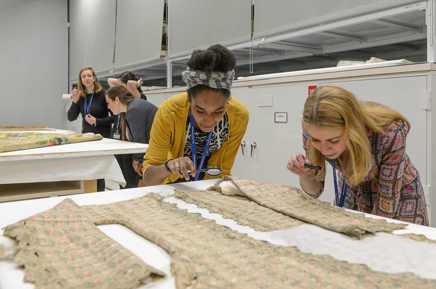 Two interns inspect a textile using magnifying glasses